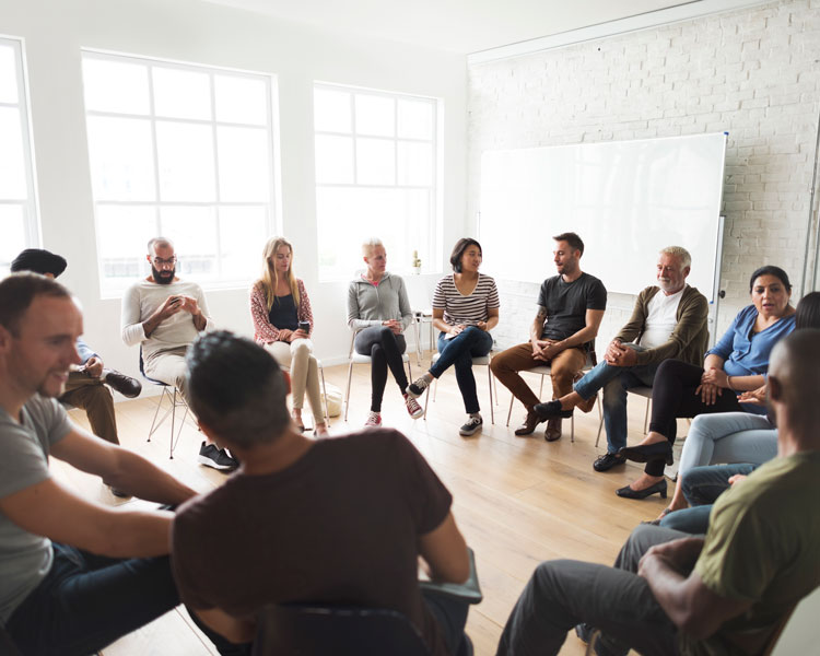A therapy group talking together in a circle of chairs in a bright room